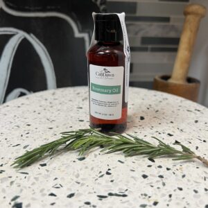 Amer bottle on pedestal stand with fresh rosemary leaves in front.