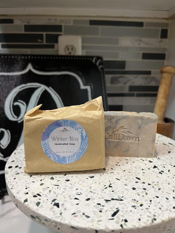 two blue and tan swirl soap bars on a pedestal stand. One in brown package with label.