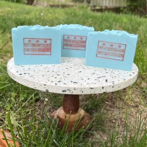 three light blue soaps with red DC flag on pedestal in yard.