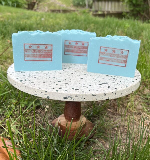 three light blue soaps with red DC flag on pedestal in yard.